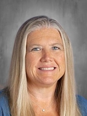 Portrait of a woman with long, straight blonde hair, smiling warmly, wearing a blue top, against a neutral background.