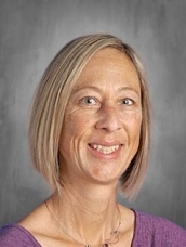 Retrato de una mujer con cabello corto y castaño claro, sonriendo, con una camisa morada, sobre un fondo gris.