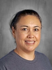 Smiling woman with medium-length dark hair, wearing a gray shirt, against a neutral background.