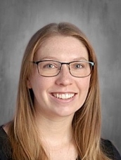 Smiling woman with long blonde hair and glasses, wearing a black top, set against a neutral background.