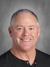 Smiling man with short gray hair wearing a black shirt, set against a neutral background.
