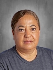A woman with short, wavy hair wearing a gray shirt, looking directly at the camera against a plain background.