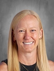 Smiling woman with long blonde hair, wearing a black top, against a gray background.