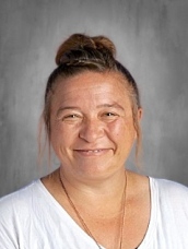 Smiling woman with a bun hairstyle, wearing a white shirt, against a neutral gray background.