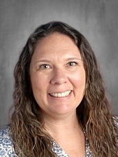 Smiling woman with long, wavy hair wearing a patterned blouse, set against a neutral background.
