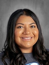 Smiling woman with long black hair, wearing a gray shirt, against a neutral background.