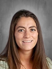 Portrait of a smiling woman with long brown hair, wearing a light green top, against a gray background.