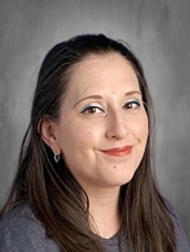 Portrait of a woman with long dark hair and a warm smile, wearing a gray shirt against a neutral background.