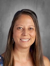 Smiling woman with long brown hair, wearing a patterned top, set against a neutral background.