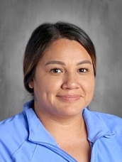 Smiling woman with medium brown hair wearing a blue jacket, set against a gray background.