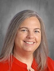 Smiling woman with long gray hair wearing a red blouse, set against a neutral background.