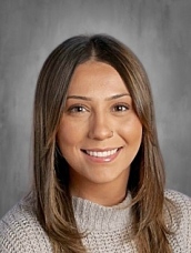 Smiling woman with long brown hair wearing a light sweater, set against a neutral gray background.