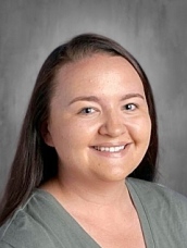 Smiling woman with long, dark hair, wearing a gray shirt, against a plain background.