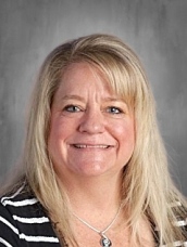 A smiling woman with long blonde hair, wearing a striped shirt, against a neutral background.