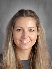 Headshot of a smiling woman with long, straight hair, wearing a dark shirt, against a neutral gray background.
