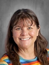 Smiling woman with long brown hair wearing a colorful striped shirt against a gray background.