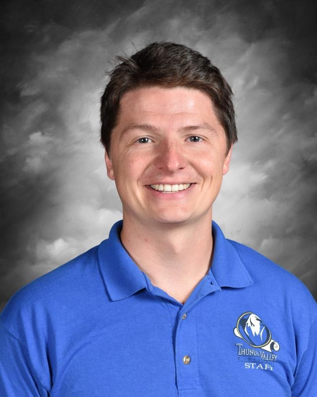 Smiling person in a blue Thunder Valley Staff polo, against a cloudy gray background.