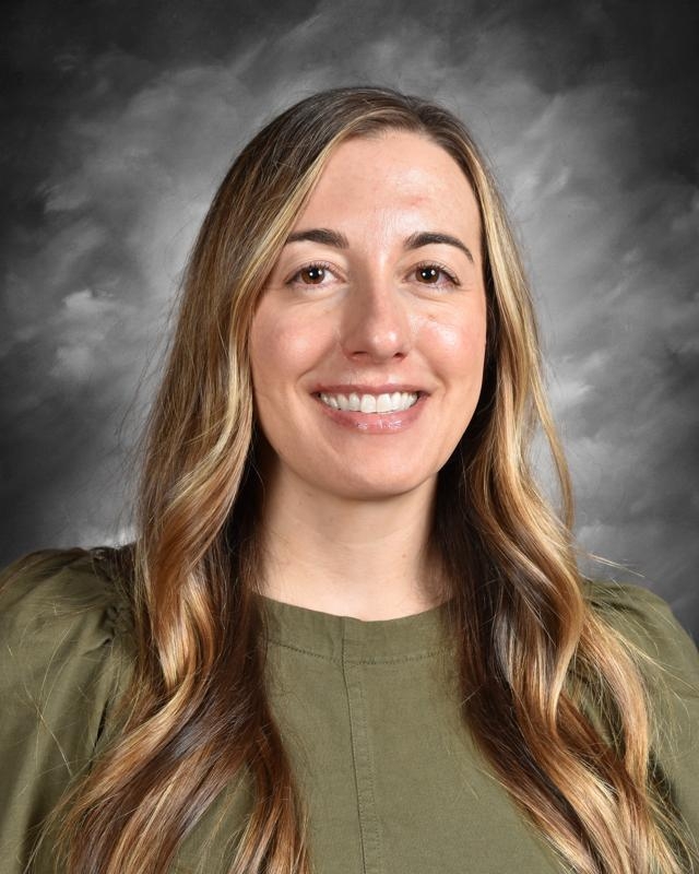 Smiling person with long hair in a green top, against a gray background.